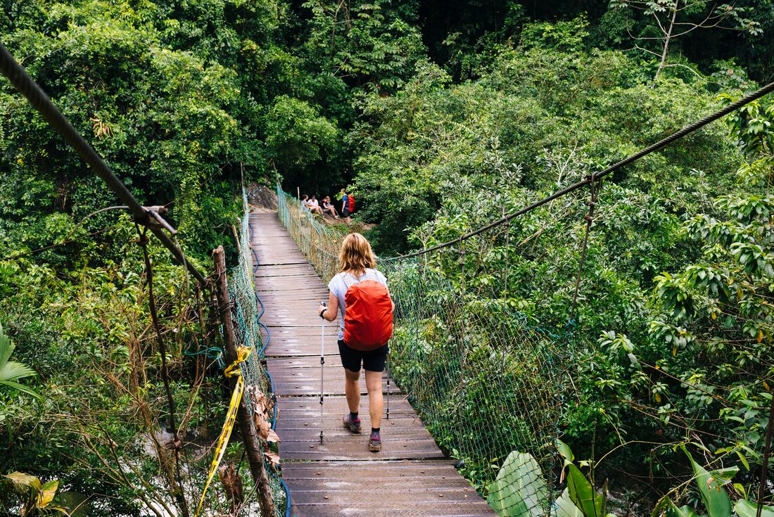 Traveller with red backpack crossing a bridged river on the way to Ciudad Perdida or the Lost City