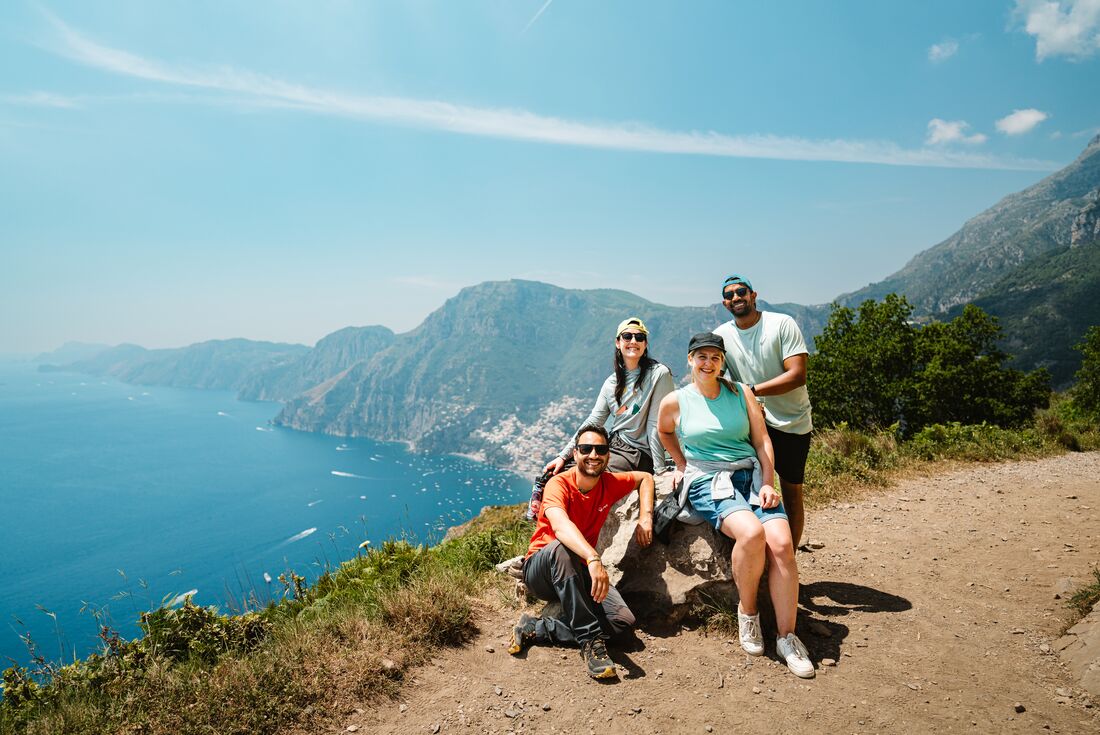Travellers take a photo with Leader on a cliffside trail overlooking the blue sea and mountains of the Amalfi Coast, Italy